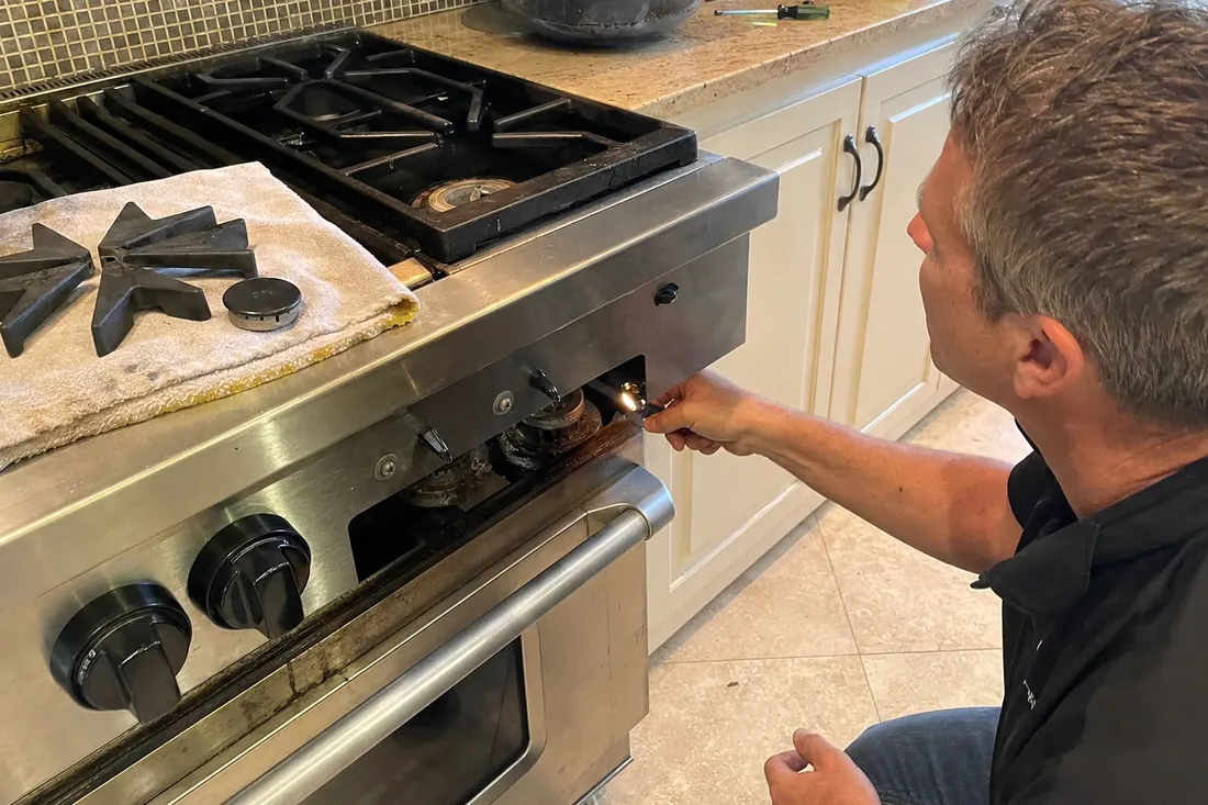Technician checking the igniter on a dual-fuel range, one burner cap lifted off, the exposed burner head in frame - The brands we service