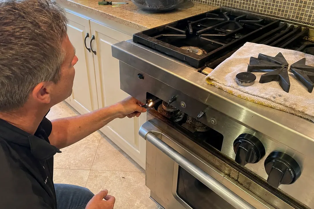 Technician checking the igniter on a dual-fuel range, one burner cap lifted off, the cast-iron grates in frame - La Cornue repair in Jacksonville and Northeast Florida