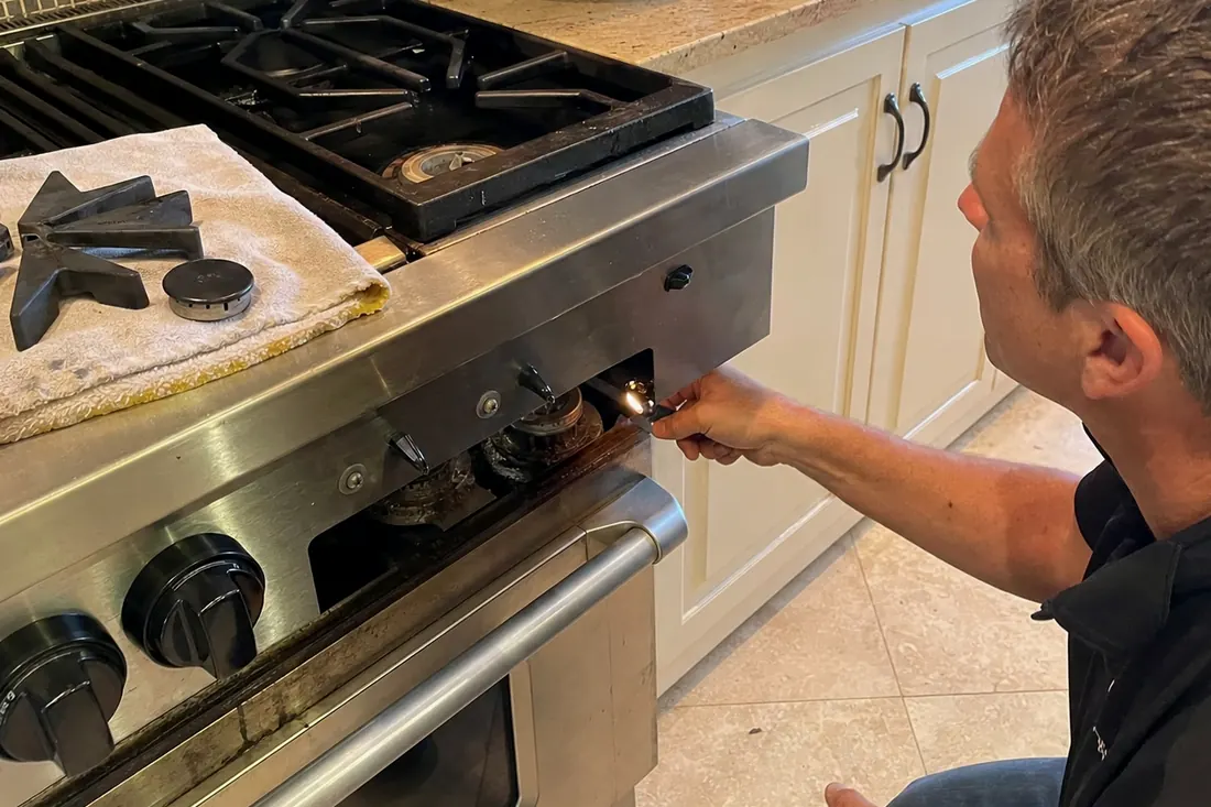 Technician checking the igniter on a dual-fuel range, one burner cap lifted off, the cast-iron grates visible in the picture - Gas Burner Keeps Clicking After It Lights?