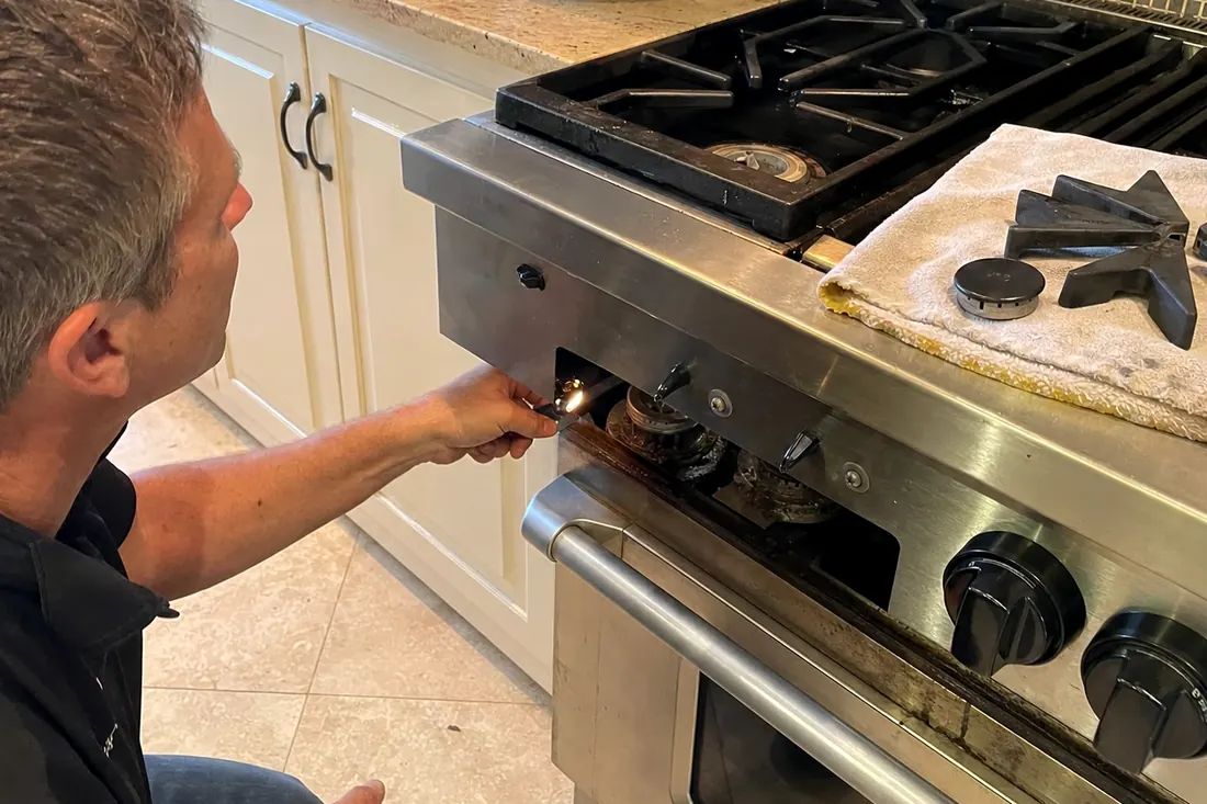 Technician checking the igniter on a dual-fuel range, one burner cap lifted off, the range front visible in the picture - Pro-Style Range Oven Not Holding Temperature?