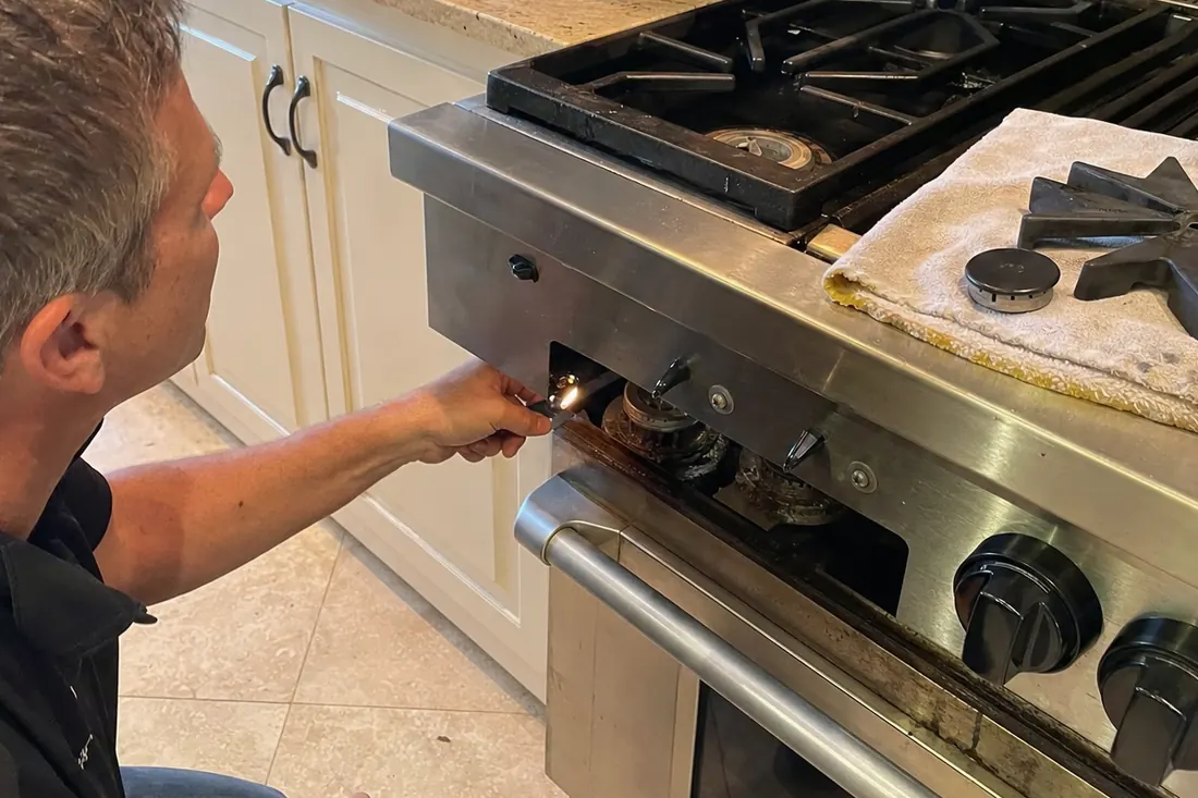 Technician checking the igniter on a dual-fuel range, one burner cap lifted off, the lifted grate in frame - Sub-Zero and luxury appliance repair in Fleming Island