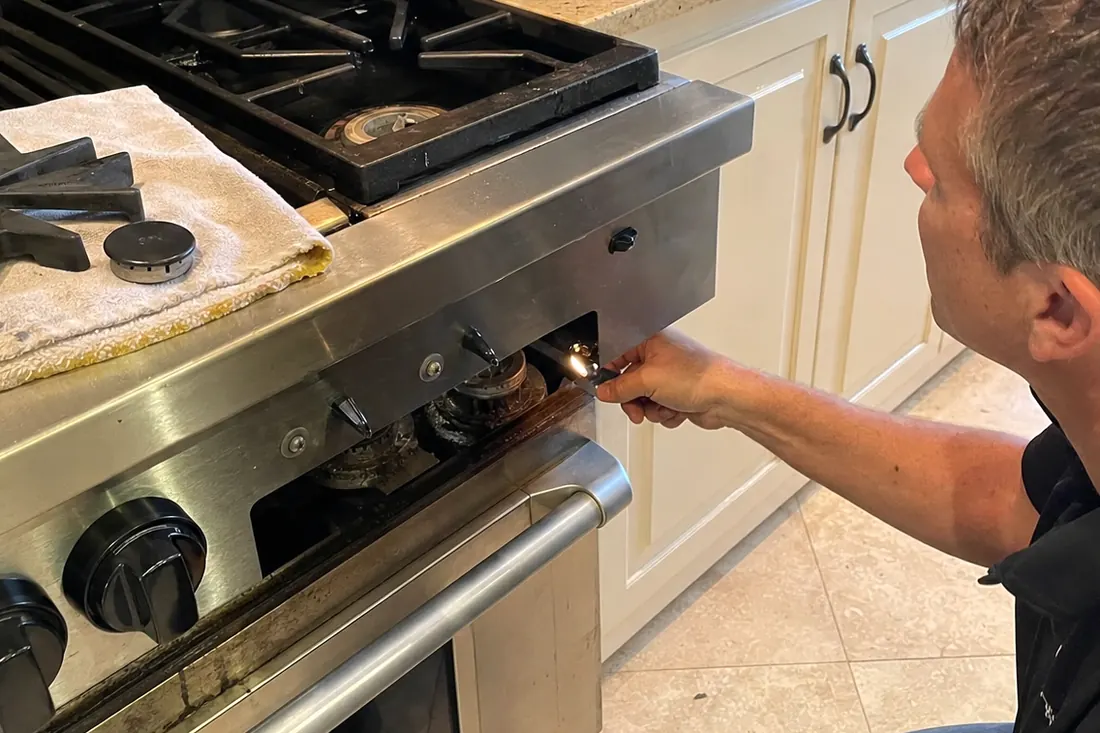 Technician checking the igniter on a dual-fuel range, one burner cap lifted off, the exposed burner head in frame - Sub-Zero and luxury appliance repair in Orange Park