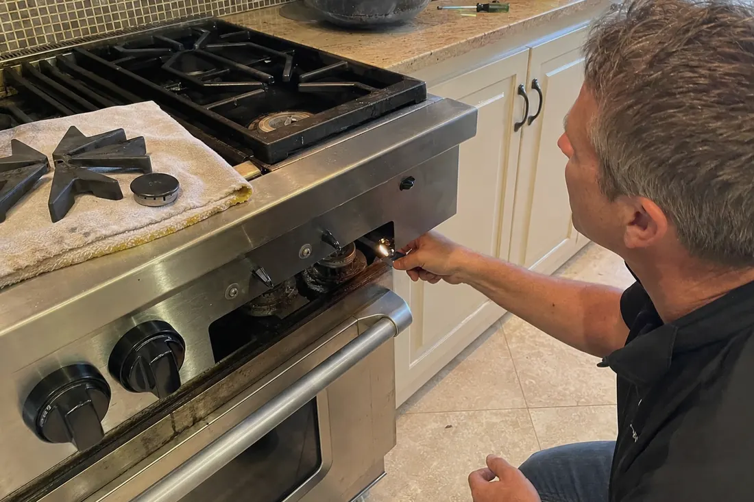 Technician checking the igniter on a dual-fuel range, one burner cap lifted off, the tile floor in frame - Range, Rangetop and Cooktop Repair
