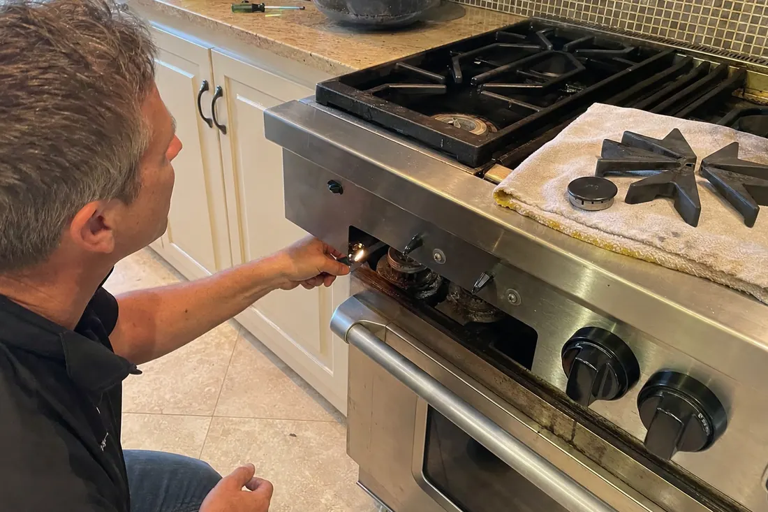 Technician checking the igniter on a dual-fuel range, one burner cap lifted off, the lifted grate visible in the picture - Range Hood and Ventilation Repair