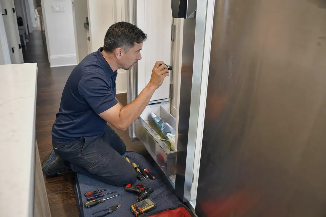 Technician checking inside an open built-in refrigerator with a flashlight - Liebherr repair in Jacksonville and Northeast Florida