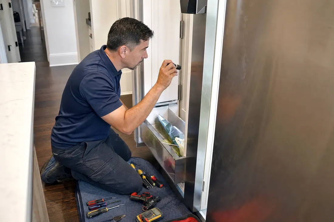 Technician checking inside an open built-in refrigerator with a flashlight, the kitchen floor in frame - Sub-Zero Showing EC50, EC40 or a Flashing SERVICE Light
