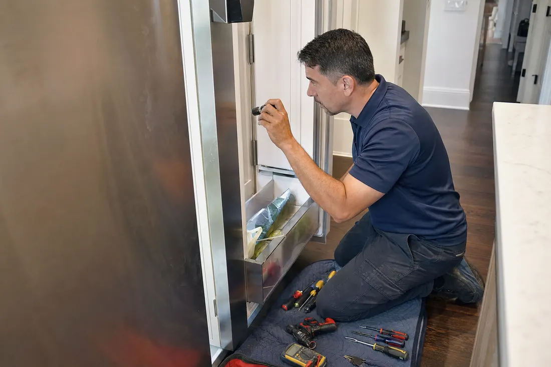 Technician checking inside an open built-in refrigerator with a flashlight, the open door visible in the picture - Sub-Zero Refrigerator Not Cooling But the Freezer Still