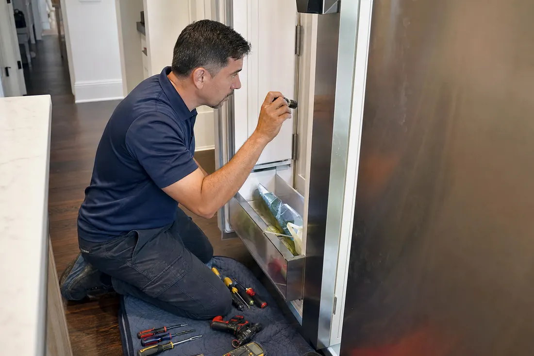 Technician checking inside an open built-in refrigerator with a flashlight, the glass shelves inside visible in the picture - Which Sub-Zero Water Filter and Air Purification