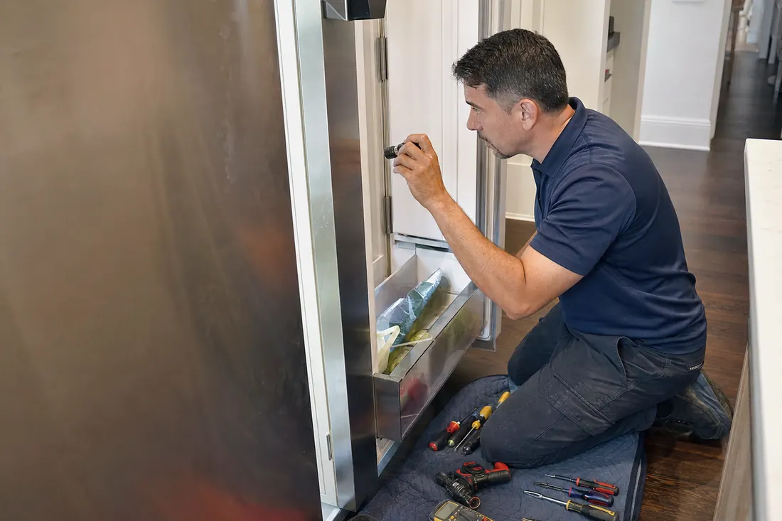 Technician checking inside an open built-in refrigerator with a flashlight, the open door in frame - Sub-Zero and luxury appliance repair in Deerwood
