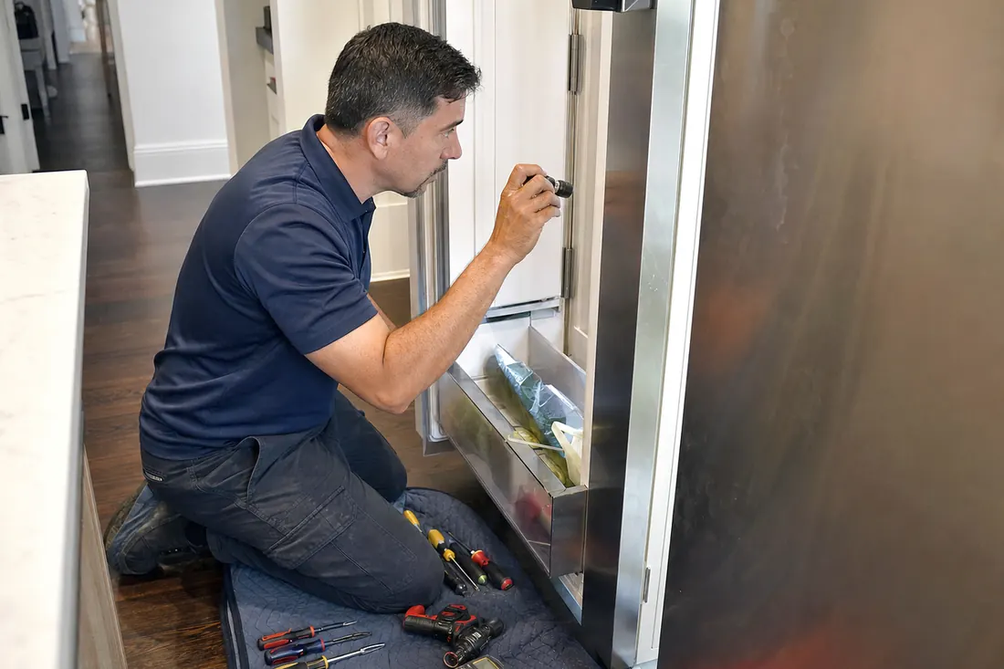 Technician checking inside an open built-in refrigerator with a flashlight, tools on a folded towel in frame - Sub-Zero and luxury appliance repair in Mandarin