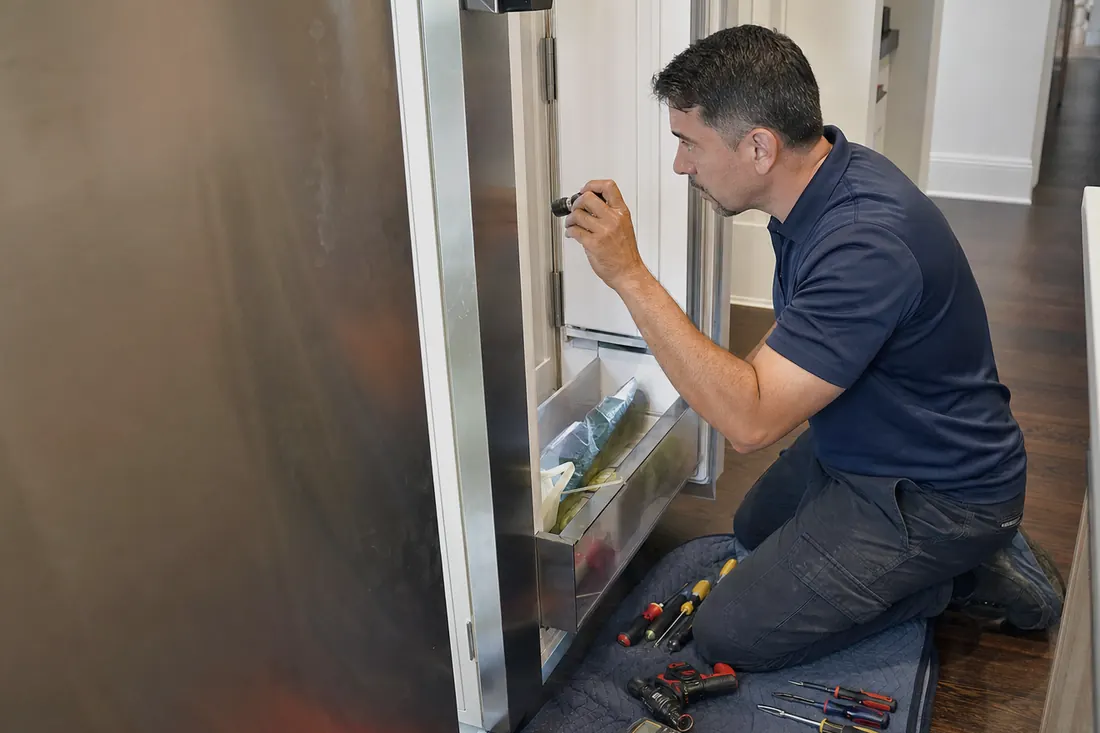 Technician checking inside an open built-in refrigerator with a flashlight, his hand steadying the door in frame - Built-In Refrigerator Repair