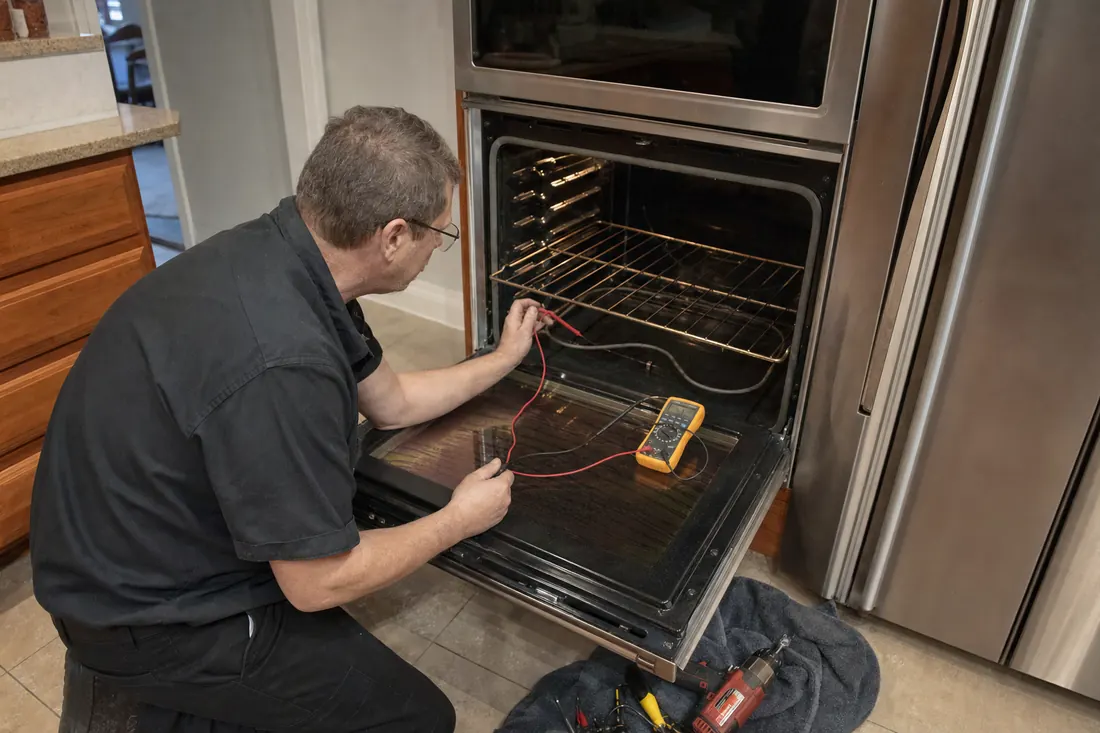 Technician testing the bake element of an open double wall oven with a multimeter, the open lower door in frame - JennAir repair in Jacksonville and Northeast Florida