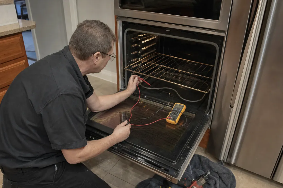 Technician testing the bake element of an open double wall oven with a multimeter, the cavity walls in frame - Built-In Coffee Systems