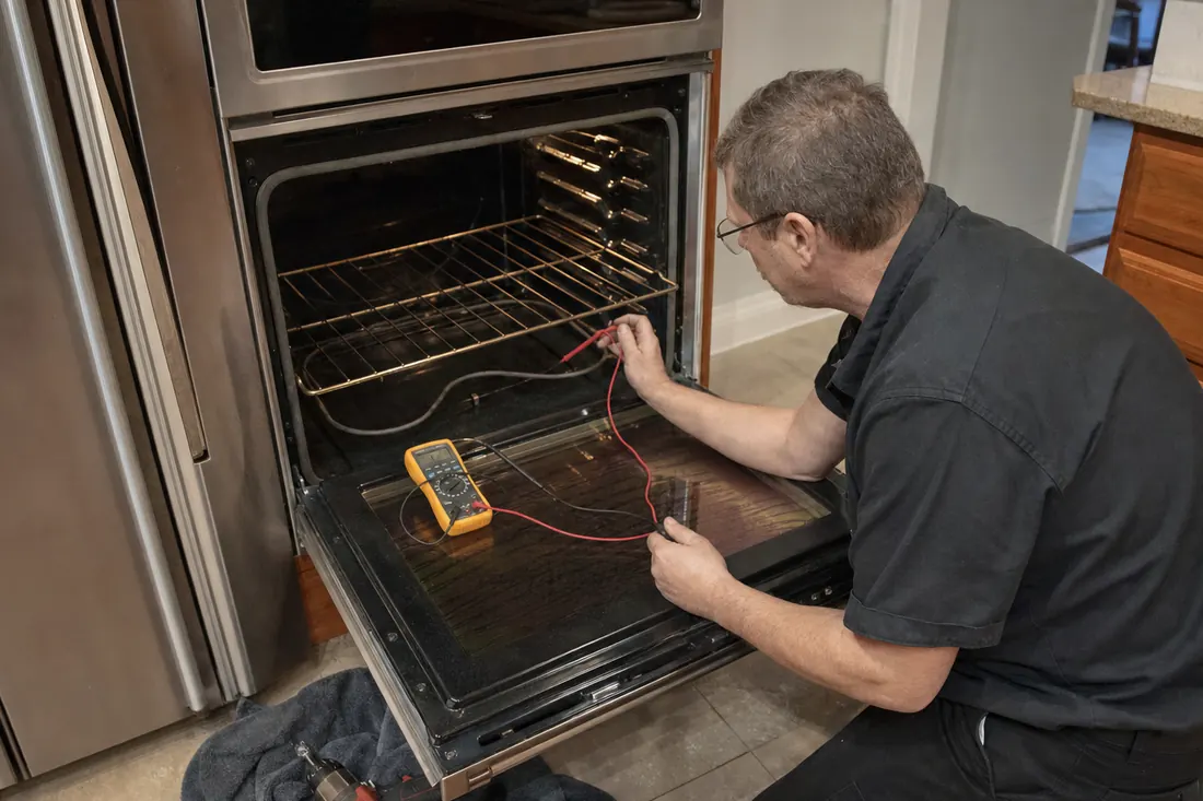 Technician testing the bake element of an open double wall oven with a multimeter, the open lower door visible in the picture - Putting Built-In Appliances Into a 1920s Kitchen