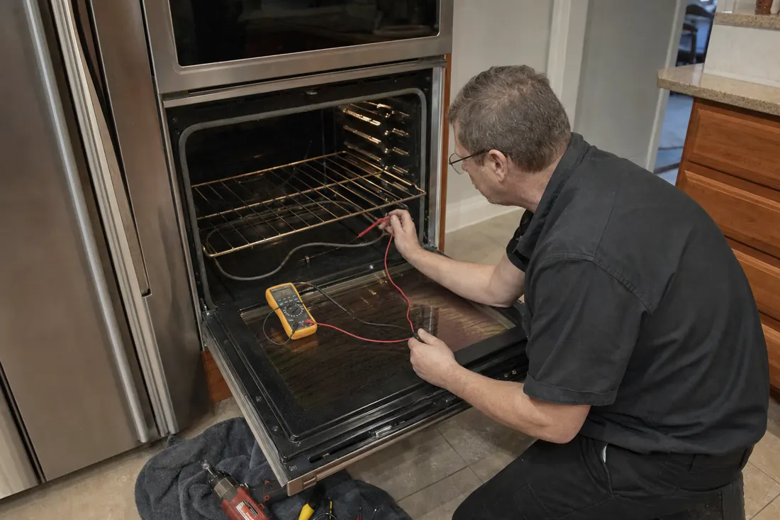 Technician testing the bake element of an open double wall oven with a multimeter, the cavity walls in frame - Appliance repair services