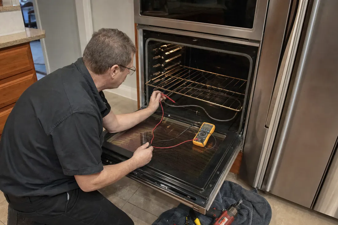 Technician testing the bake element of an open double wall oven with a multimeter, the open lower door visible in the picture - Steam Oven and Speed Oven Repair