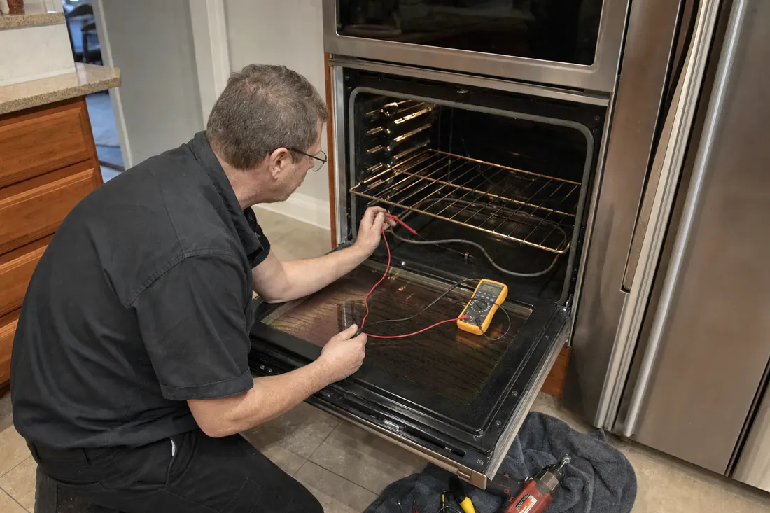 Technician testing the bake element of an open double wall oven with a multimeter, the multimeter leads visible in the picture - Built-In Wall Oven Repair